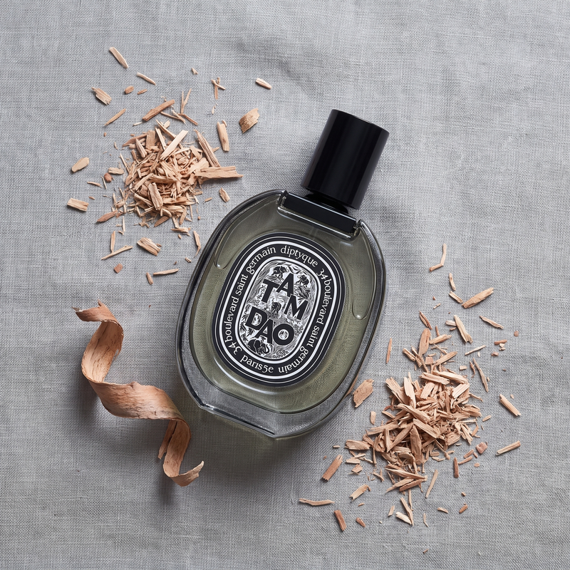 Diptyque Tam Dao Eau de Parfum on grey linen with sandalwood shavings