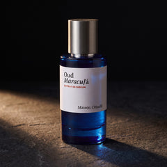 Maison Crivelli Oud Maracuja 50ml blue glass bottle lit against dark stone